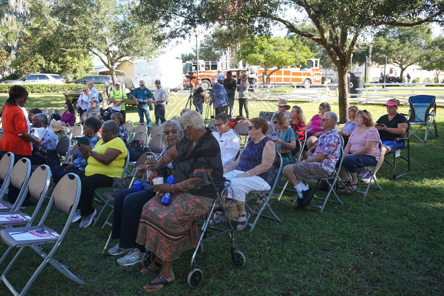 Rows of chairs set up in grass area with people sitting in the chairs wiating for the veterans day program to start