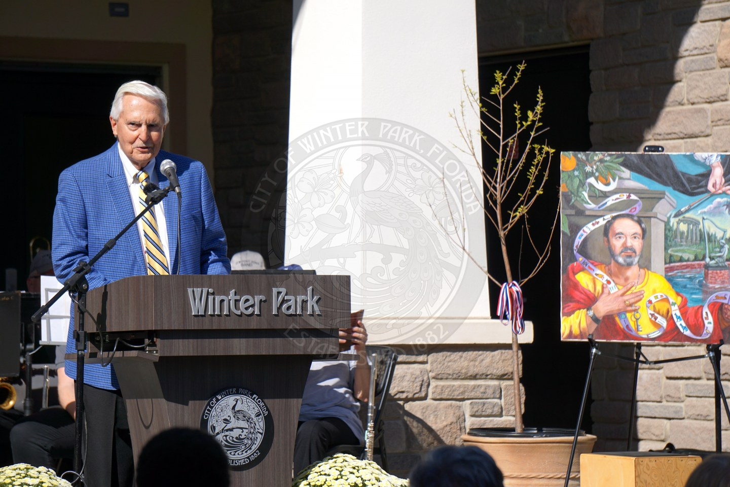 Man wearing a suit standing behind a podium that says Winter Park speaking into a mircrophone.