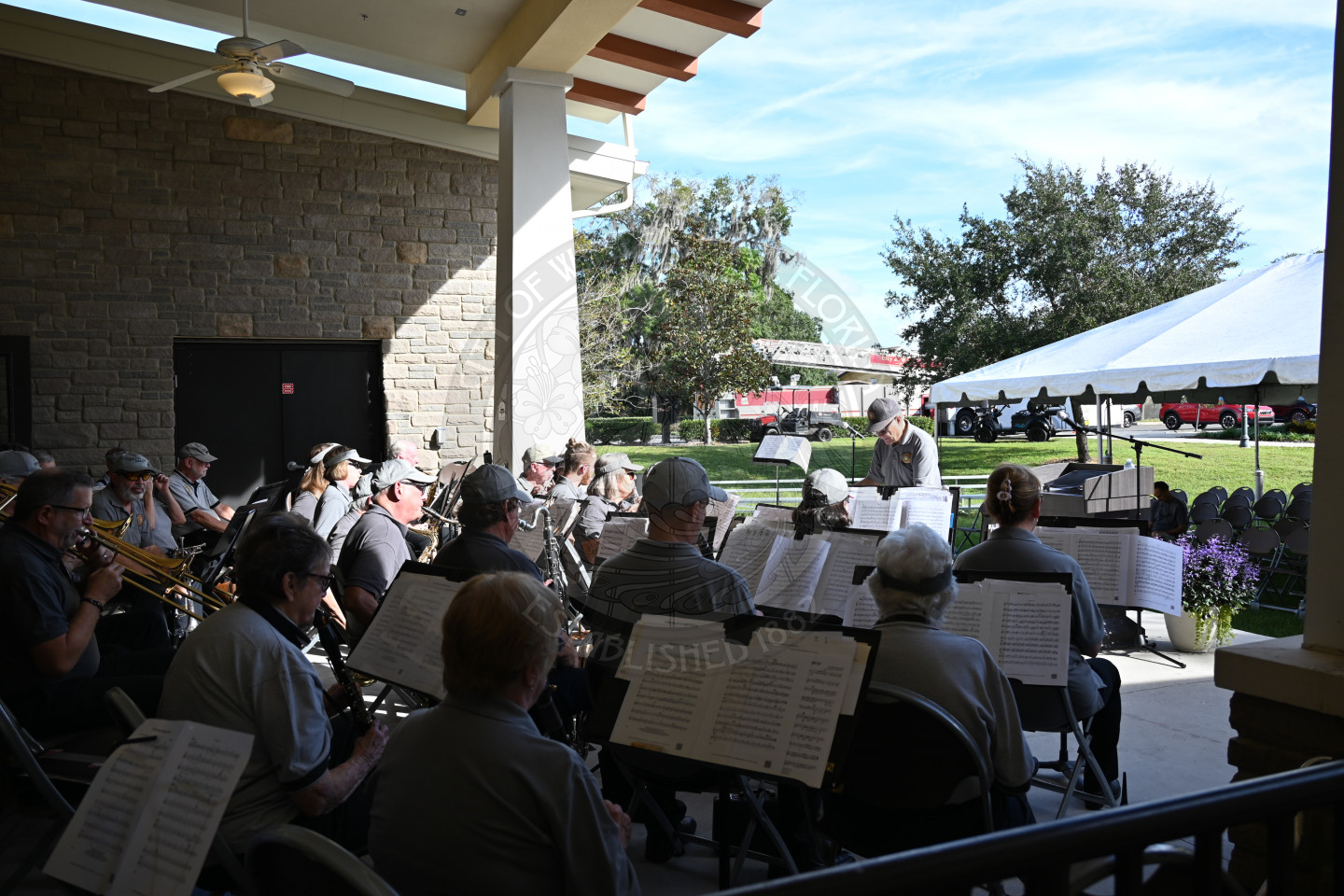 Band members sitting in chairs on a stage playing their insturments while looking at their sheet music.