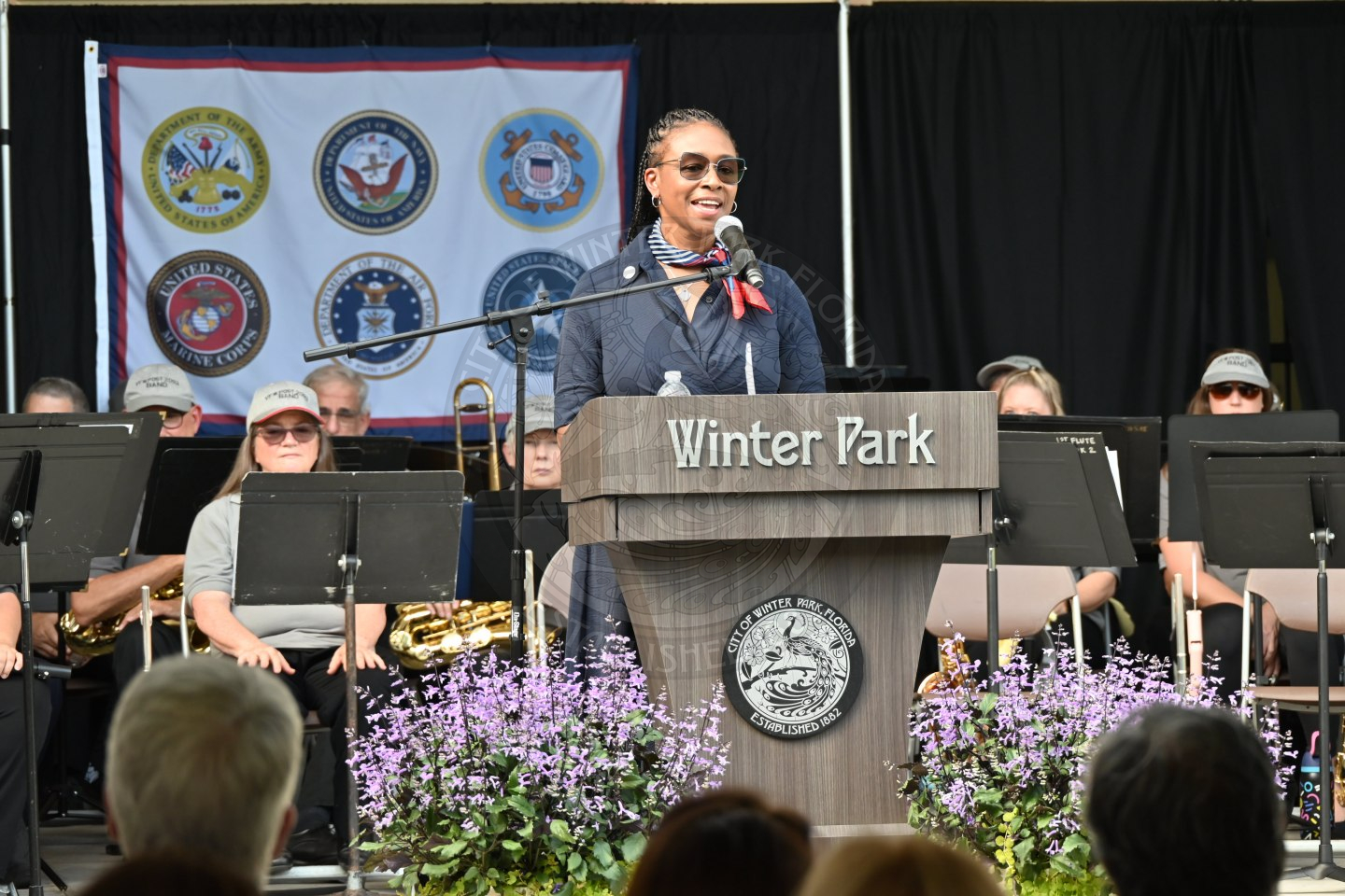 A woman speaking into a microphone and standing behind a podium that say Winter Park in front of an audience.