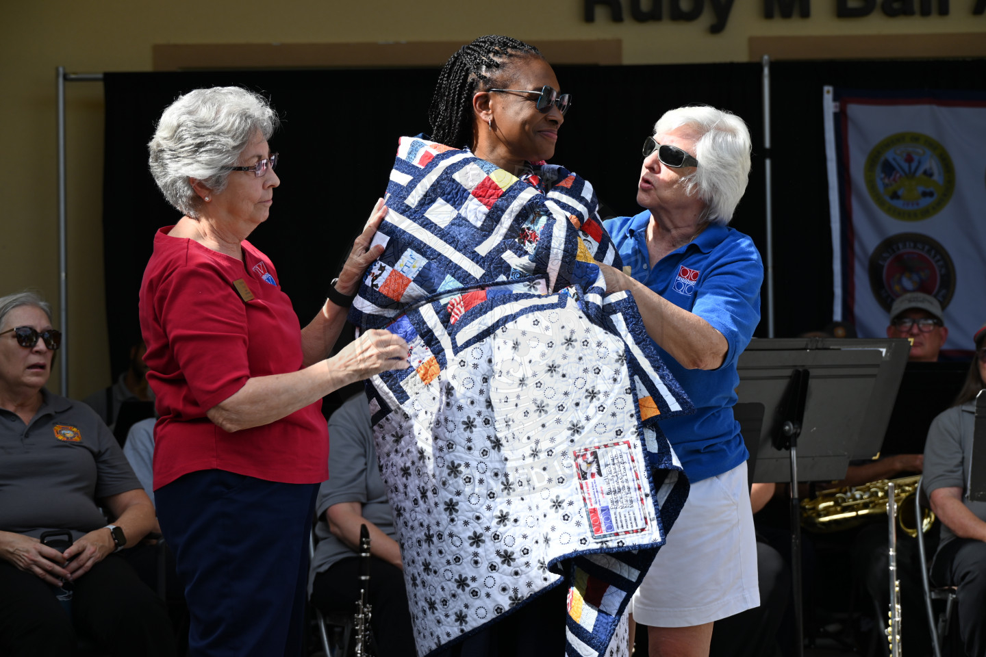 A woman standing on a stage accepting her quilt of valor being wrapped around her body.