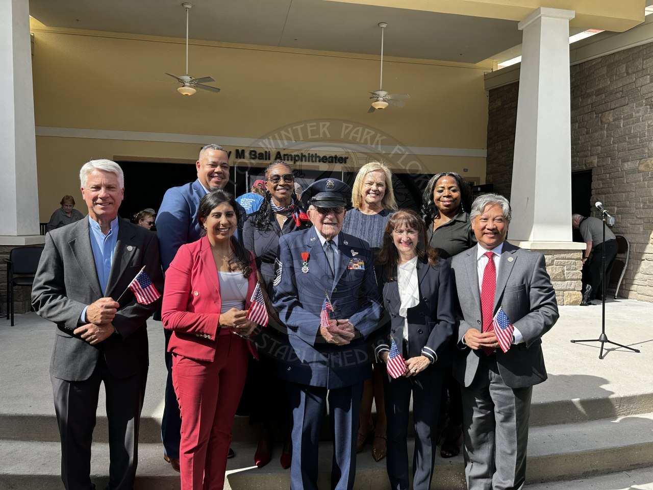 a group of elected officials and a World War II veteran standing on a stage smiling.