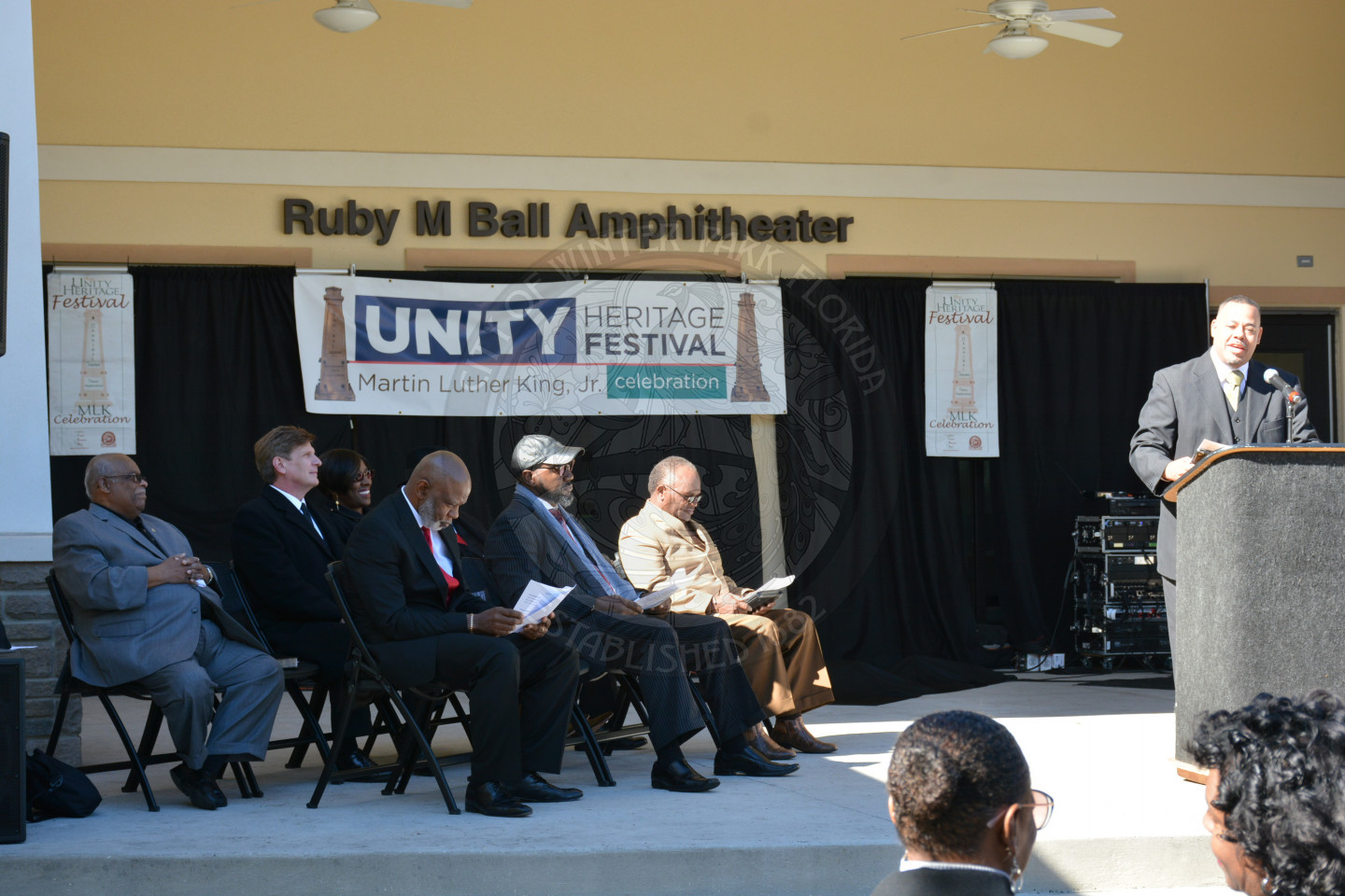Side view of the stage with VIPs seated on the stage and one gentlemen at the podium