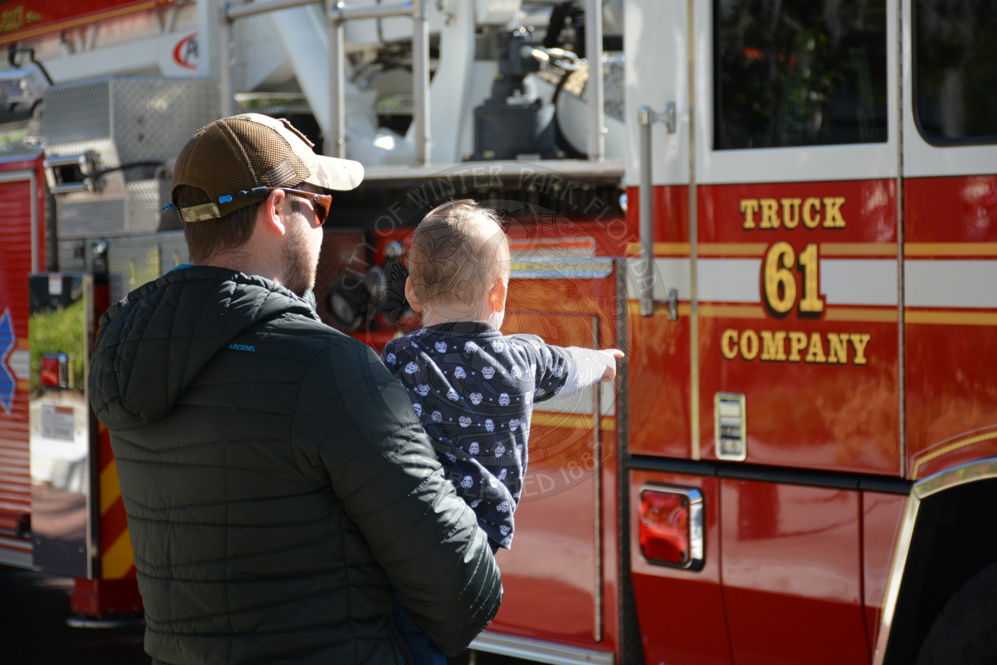 Gentleman holding young infant while looking at Fire engine 61