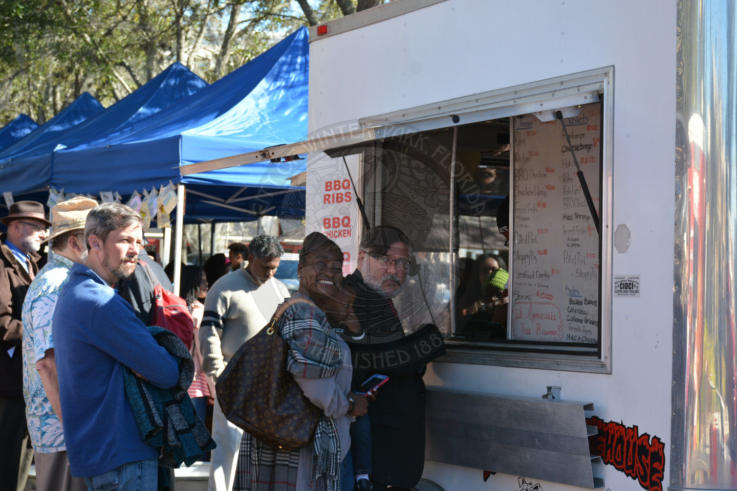 Event attendees standing in line at food vendor truck - one female smiling at camera
