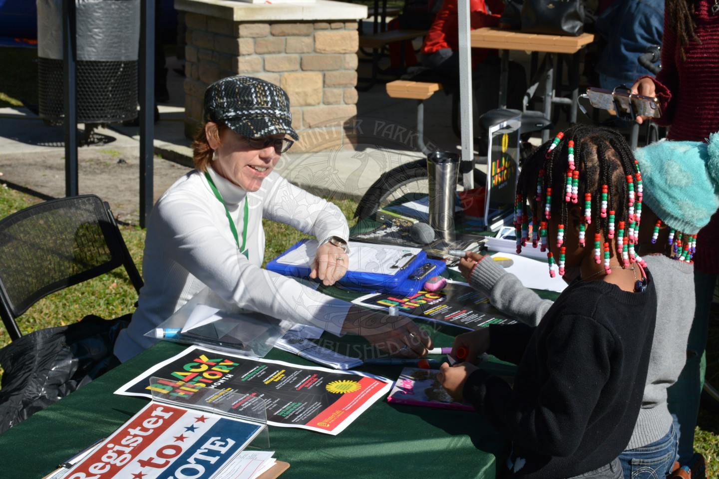 Female adult in a hat hands out materials to young girl on the other side of the table
