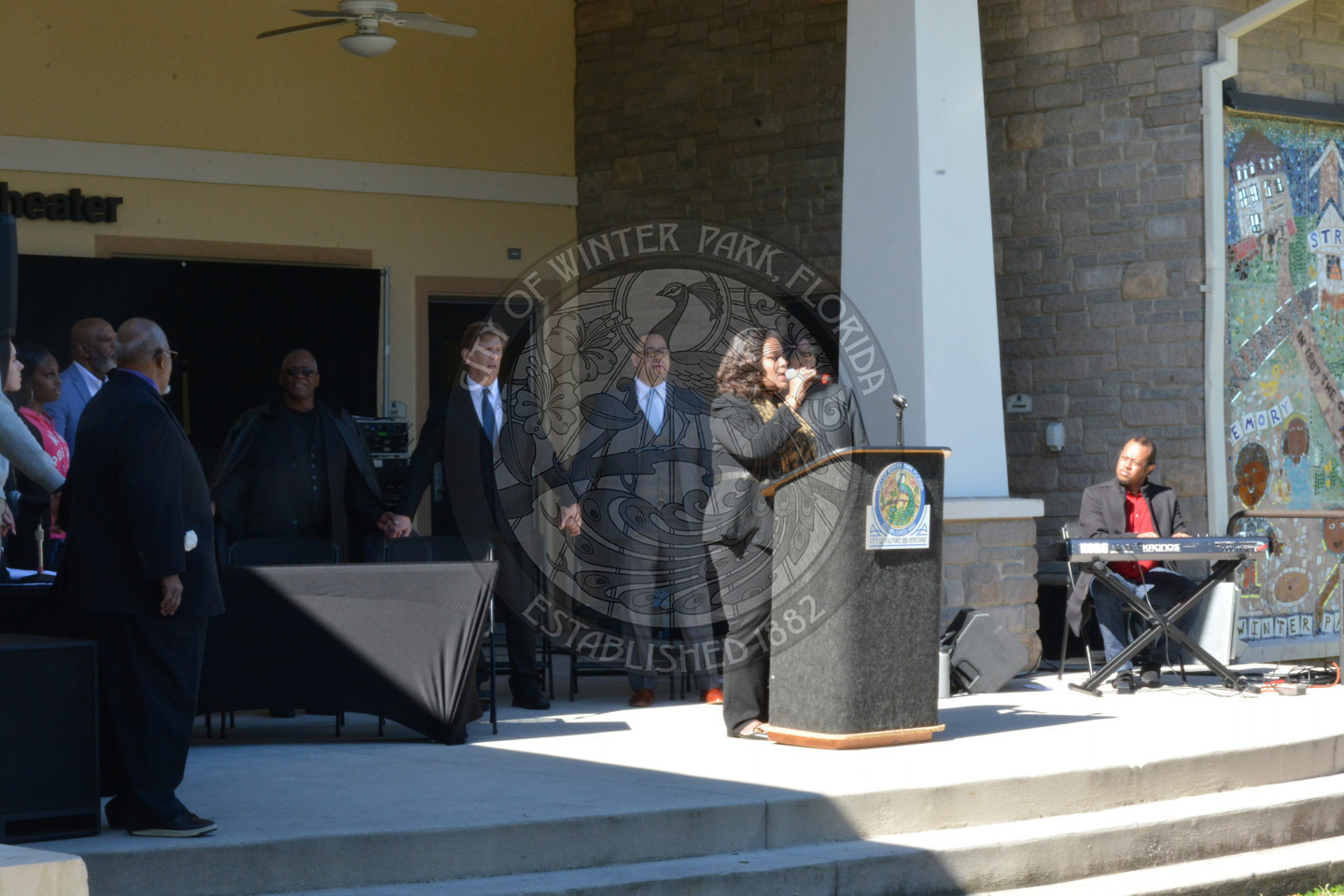 woman singing on stage behind podium and people holding hands behind her