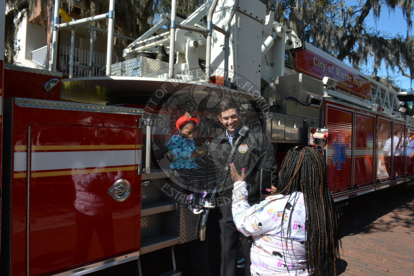 mom taking a picture of her daughter sitting on a firetruck with a firefighter