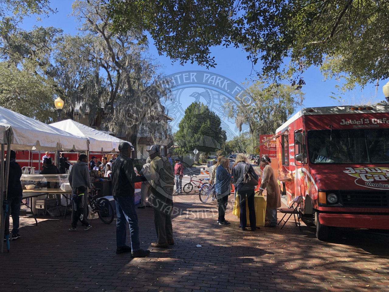 people standing in the street ordering food from vendors under tents and in a food truck