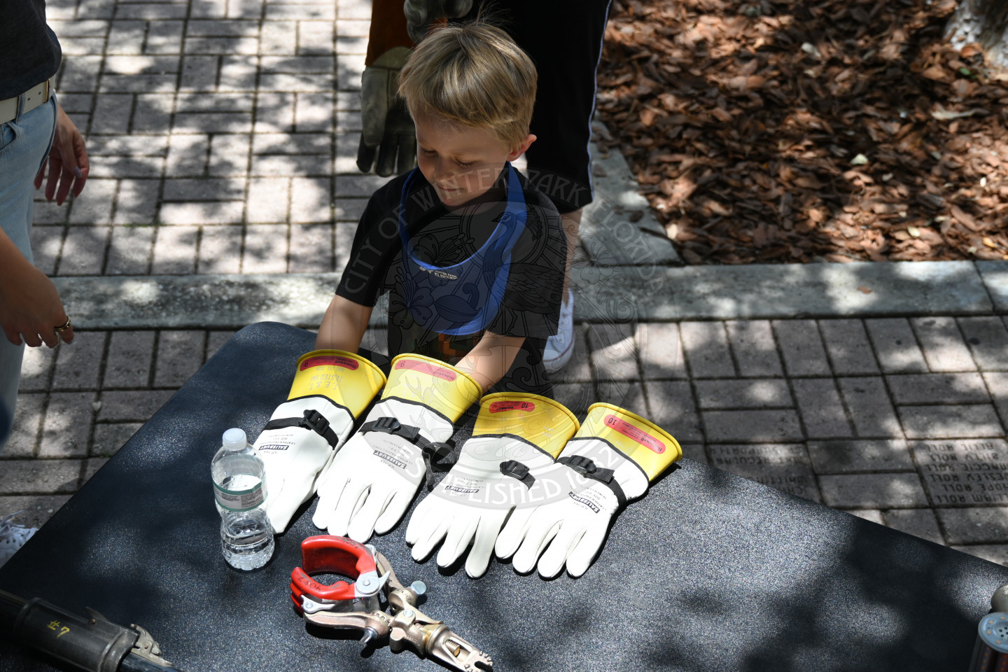 a little boy messing with a pair of adult gloves that are sitting on the table.
