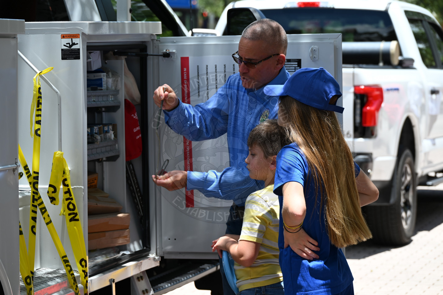an electric utility deparment worker talking to two kids about how a machine works.