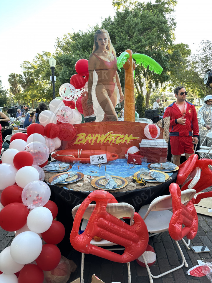 a baywatch themed table. There is a man in a red beach romper with a fanny pack.