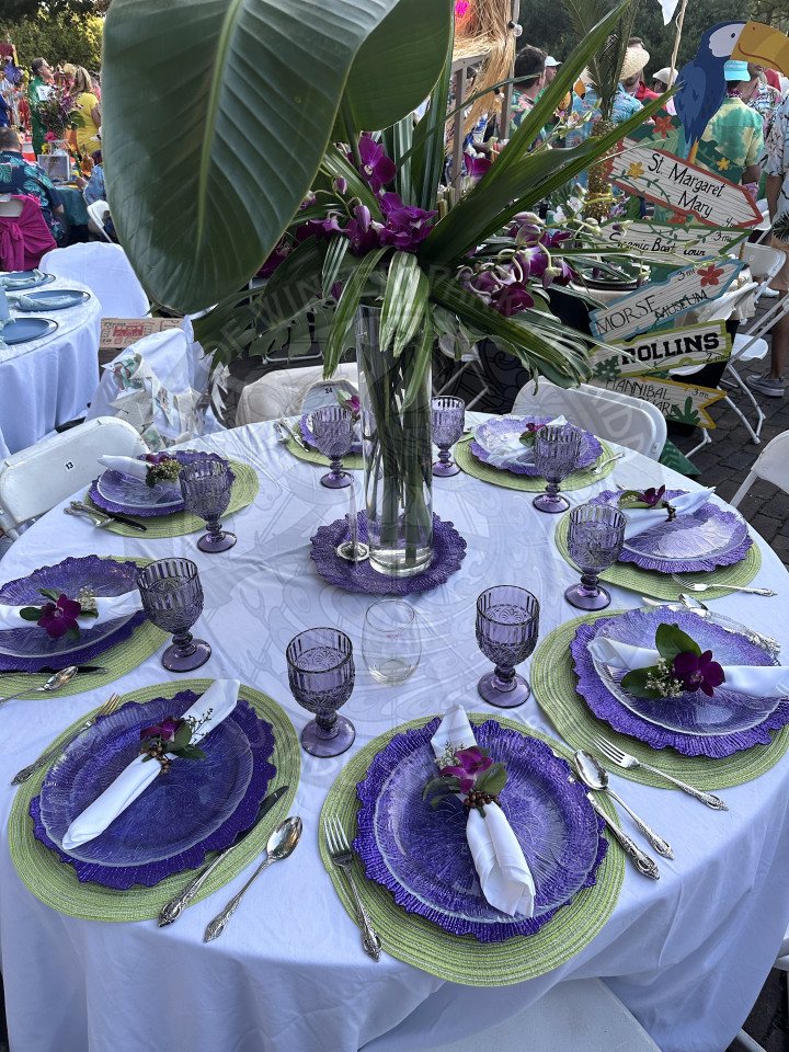 a table that had a greenery with purple plant in the middle. Around the table was purple plates and green placemats underneath.