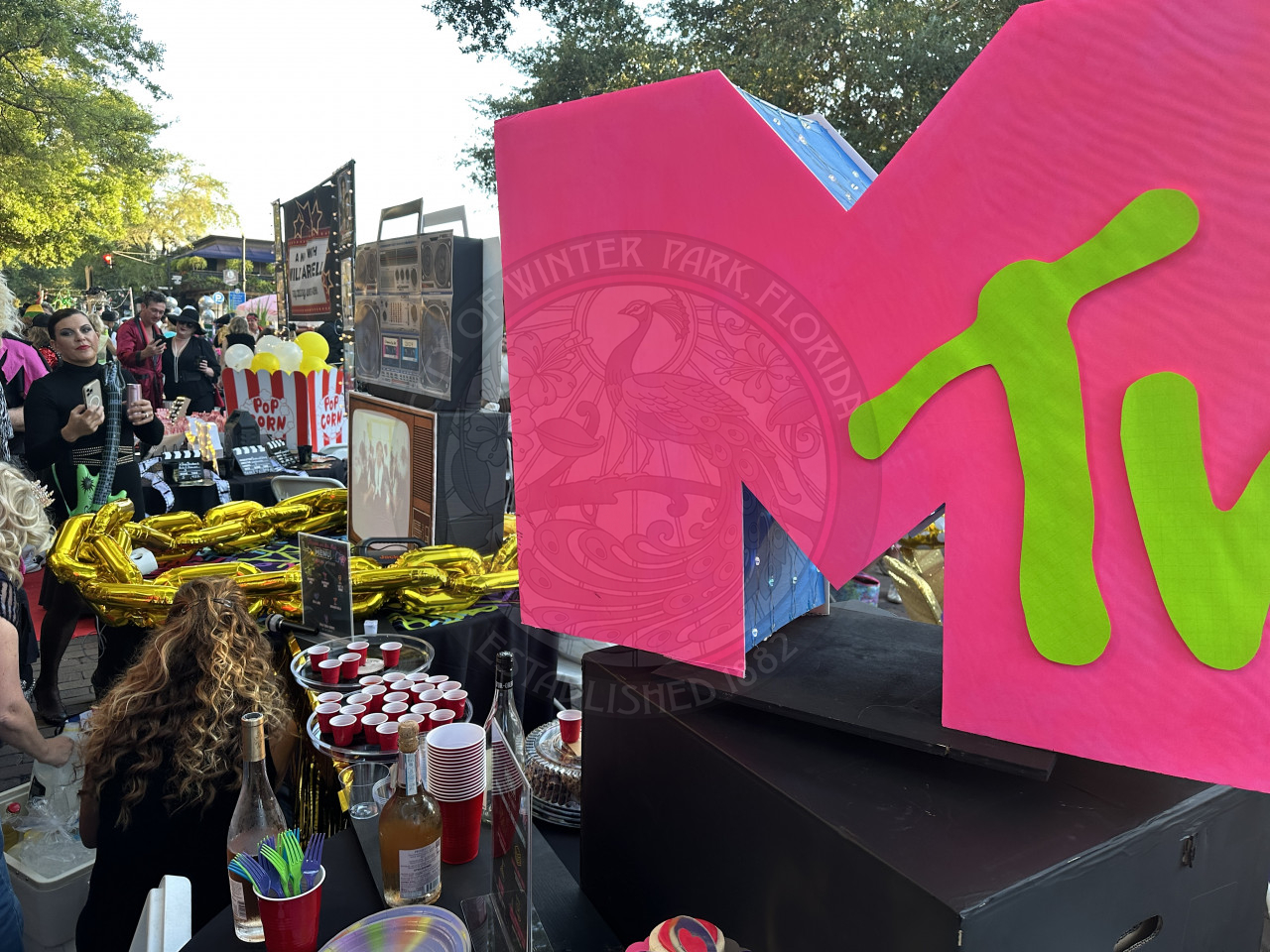 A giant homemade cardboard cutout of MTV logo. Surrounding the logo is bottles of wine and beer with red solo shot glasses.