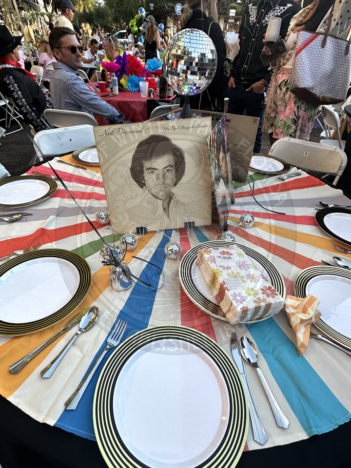 a colorful table cloth with retro plates on the table. In the middle is old vinyls and mini disco balls lined around them in a circle.