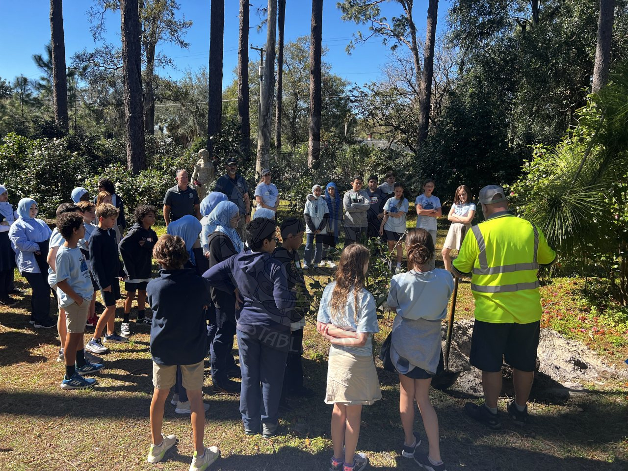 Group of kids watching city staff member teach the kids how to plant a tree