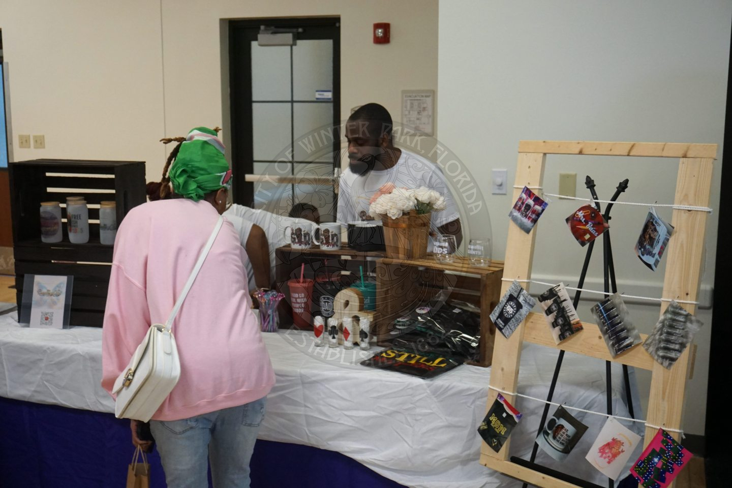 A woman looking at products for sale on a table with a man standing behind the table looking at what she is about to grab.
