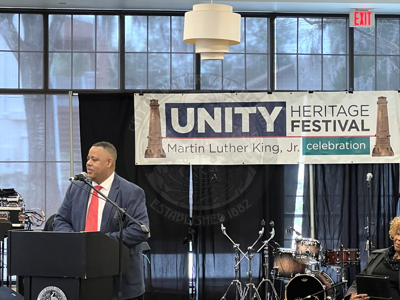 a man wearing a suit standing behind a podium with a sign in the back that says "Unity Heritage Fesitval Martin Luther King, Jr. Celebration"