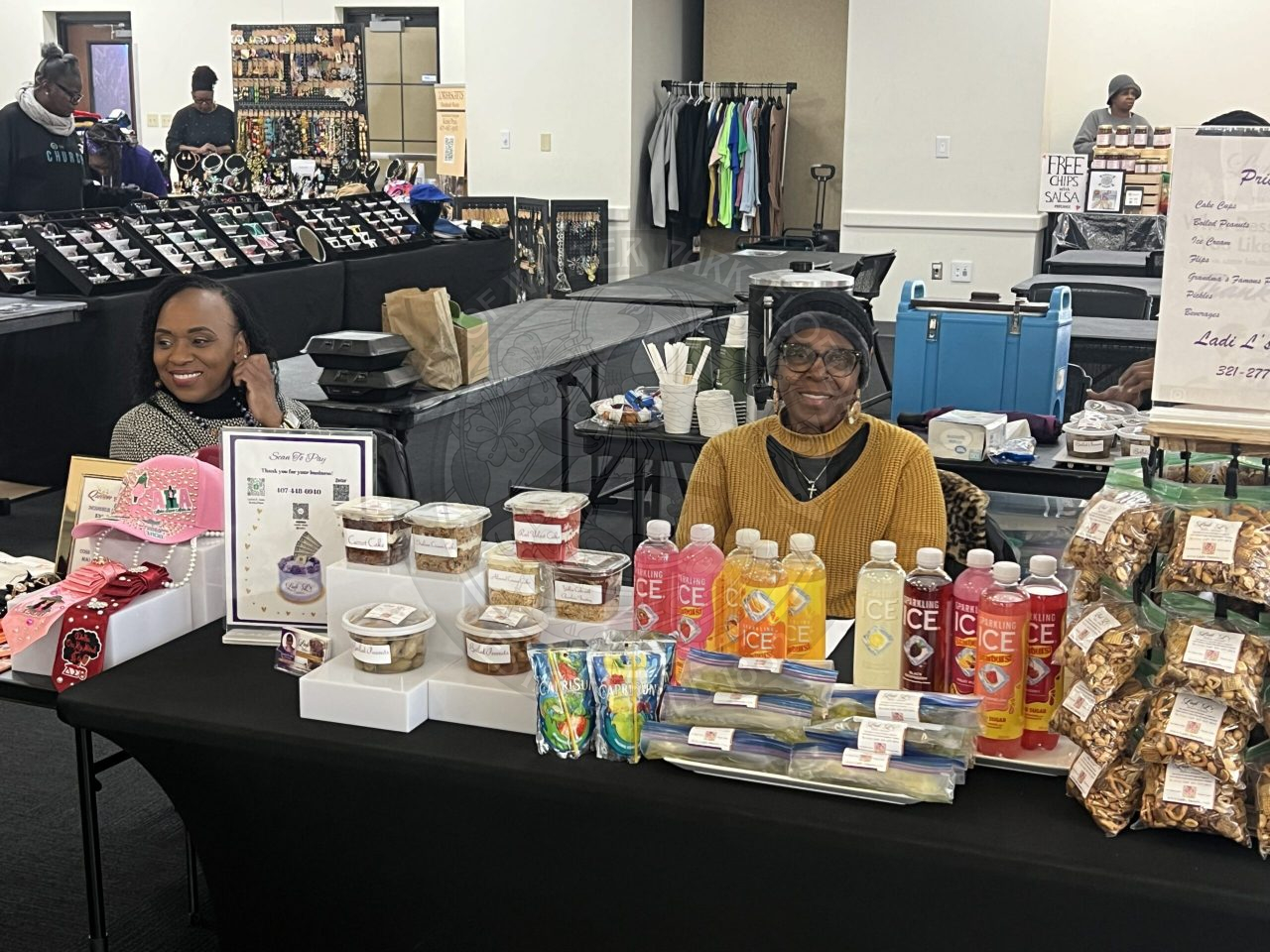 A lady sitting behind a table filled with snacks and drinks.