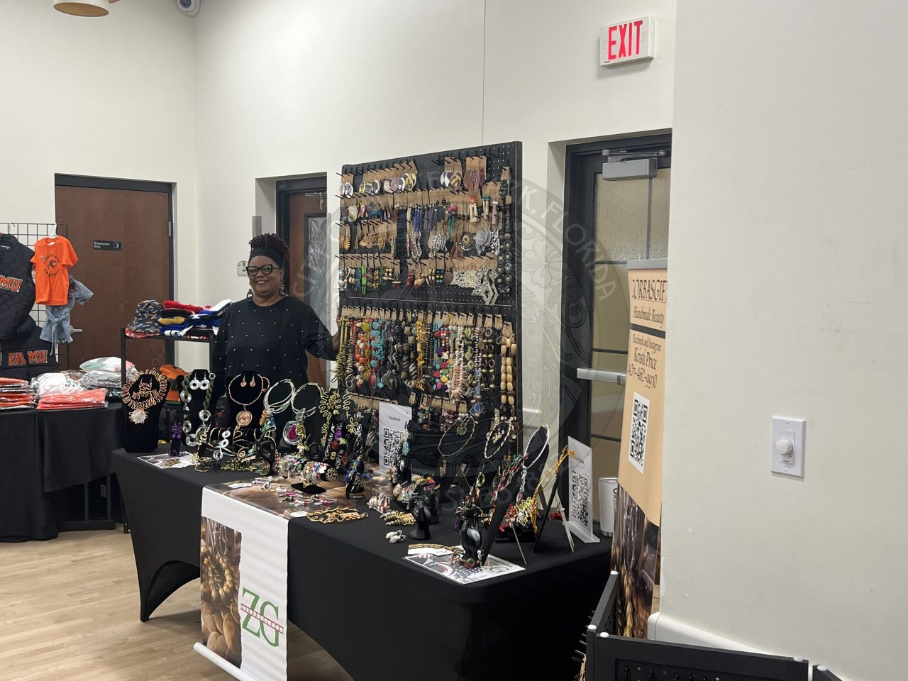 A woman standing next to a table with her products of jewelry on it.