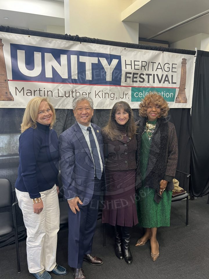 women and men standing next to each other smiling and standing underneath a banner that says "Unity Heritage Fesitval"