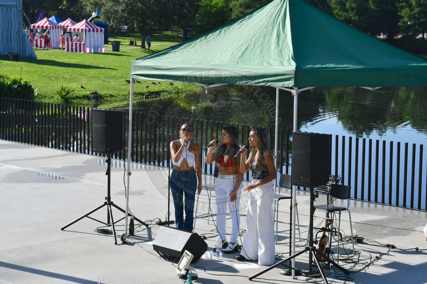 Three girls holding and singing into microphones under a tent.