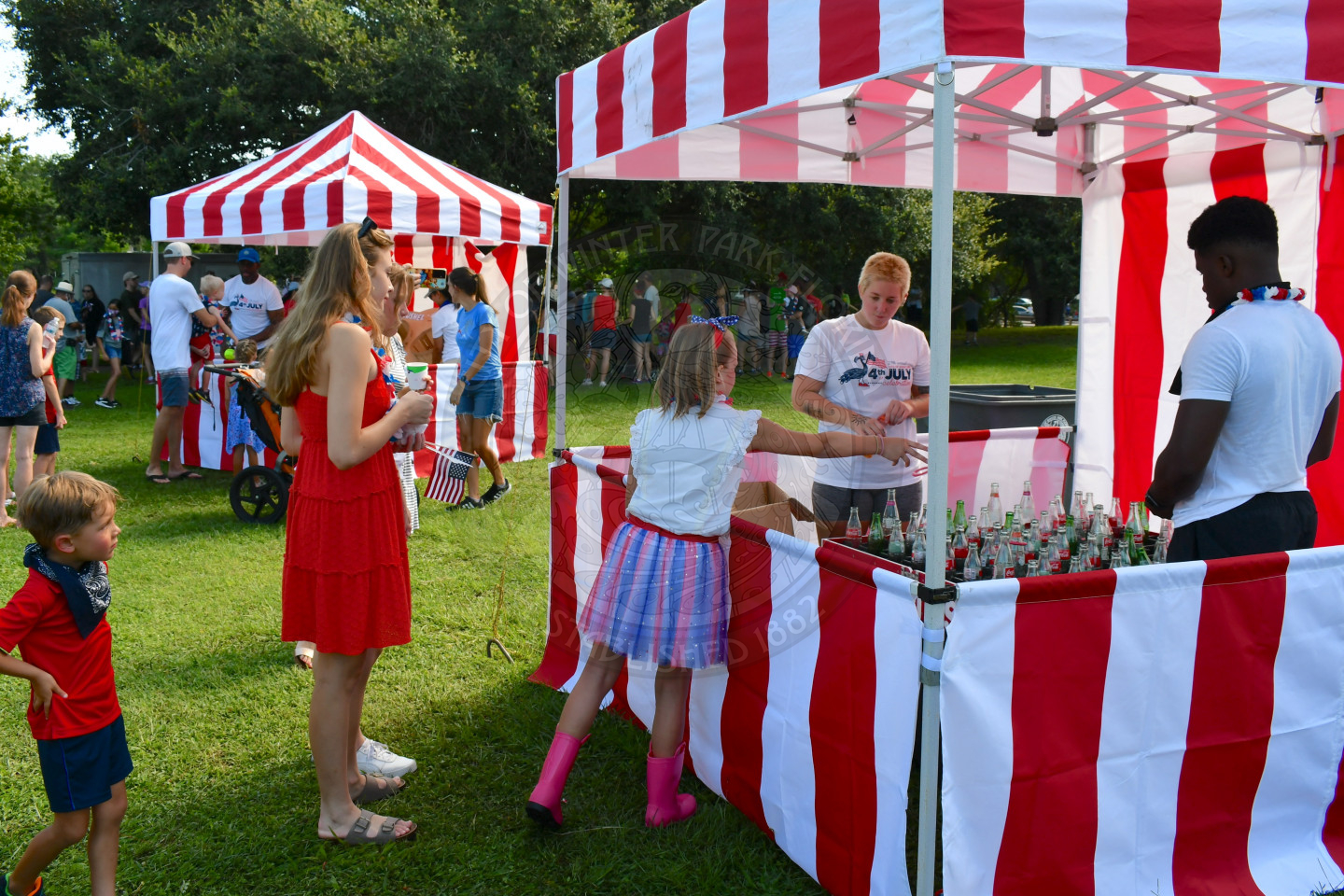 Girl throwing a ring onto a glass bottle under a tent.