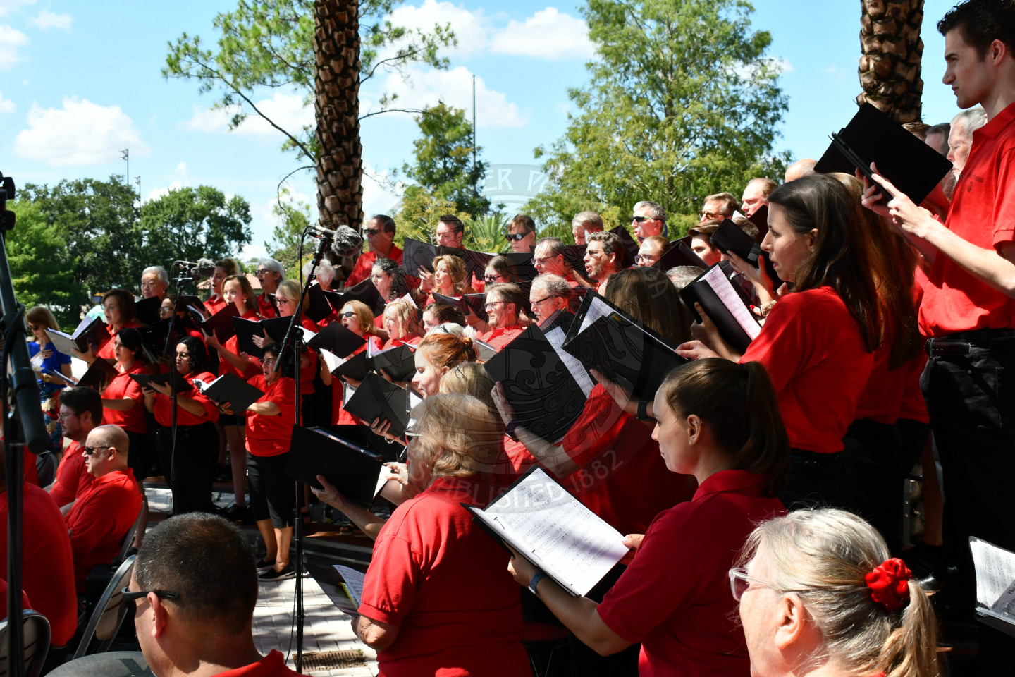 Men and women standing on the bleachers holding music sheets and singing.