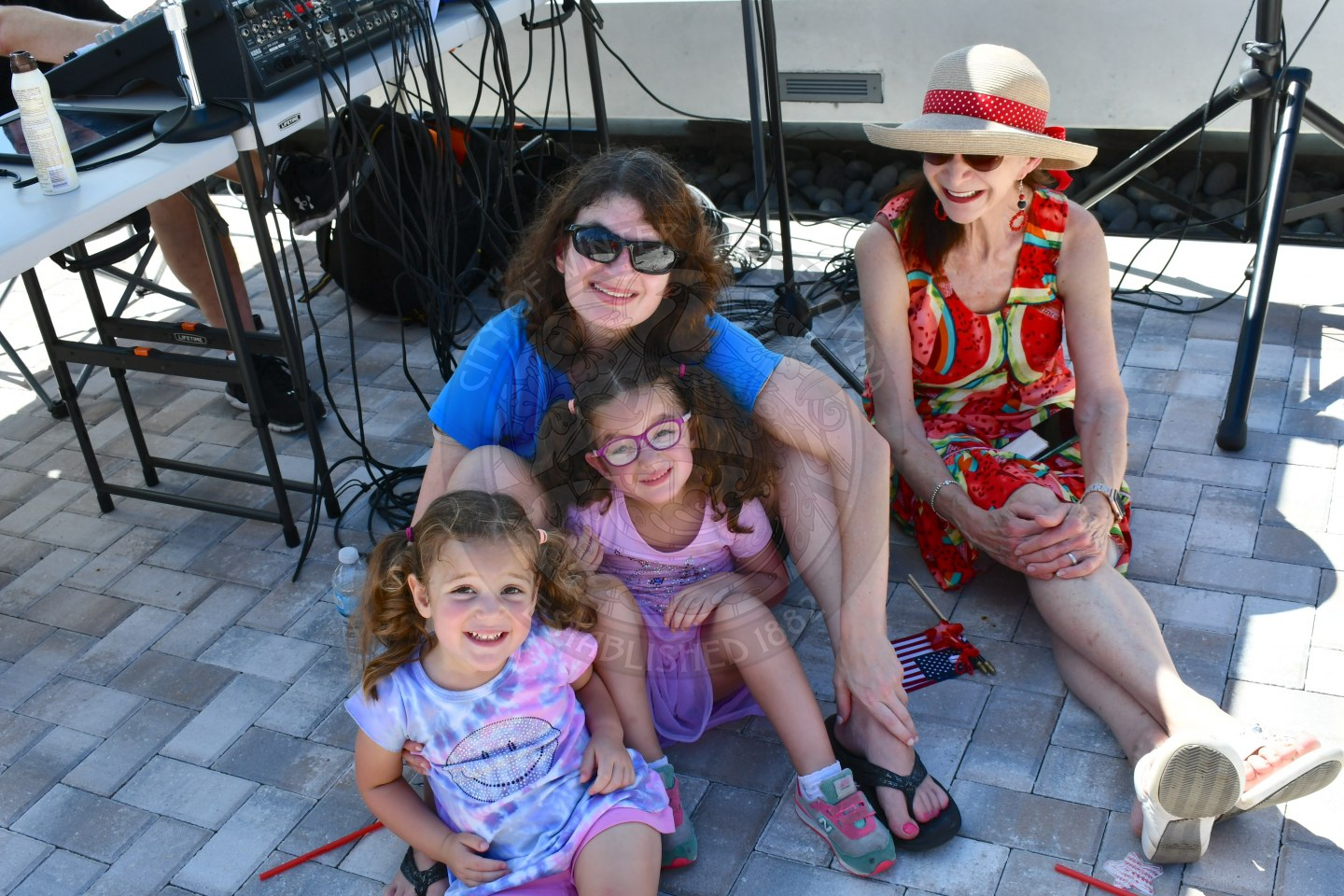 Two women and two children sitting on the ground smiling at the camera on a sunny day.