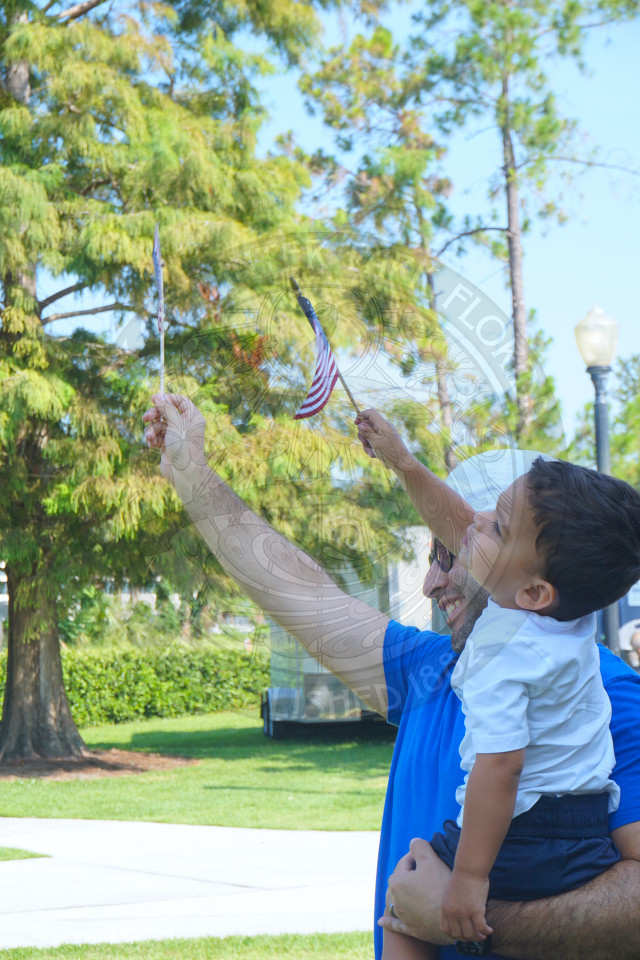 man holding a little boy while waving american flags