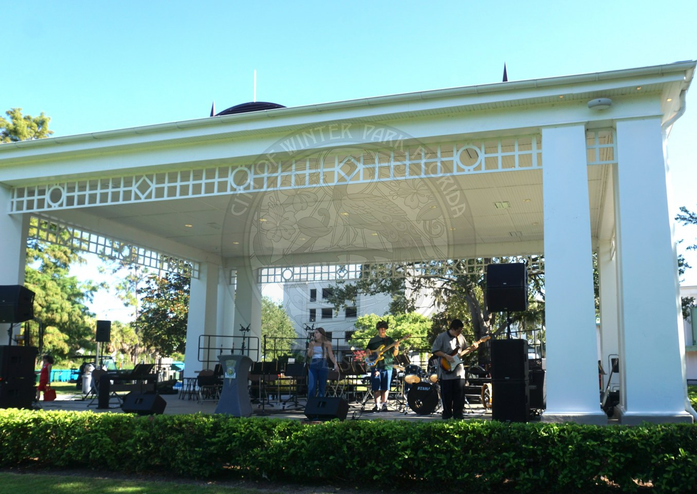 A band on the Central Park stage with a girl singing into a microphone, 2 guitarists, and a drum player.