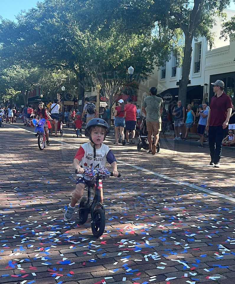 little boy riding his bike wearing red, white and blue for the fourth of july bike parade.