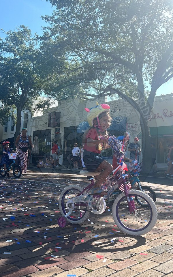 Little girl with a unicorn helmet riding her bike with training wheels. 