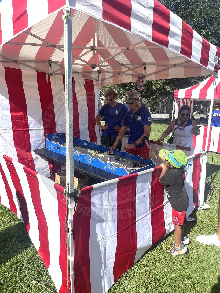 Carnival game tent with a game in the middle with a kids outside of the tent playing with the game. 