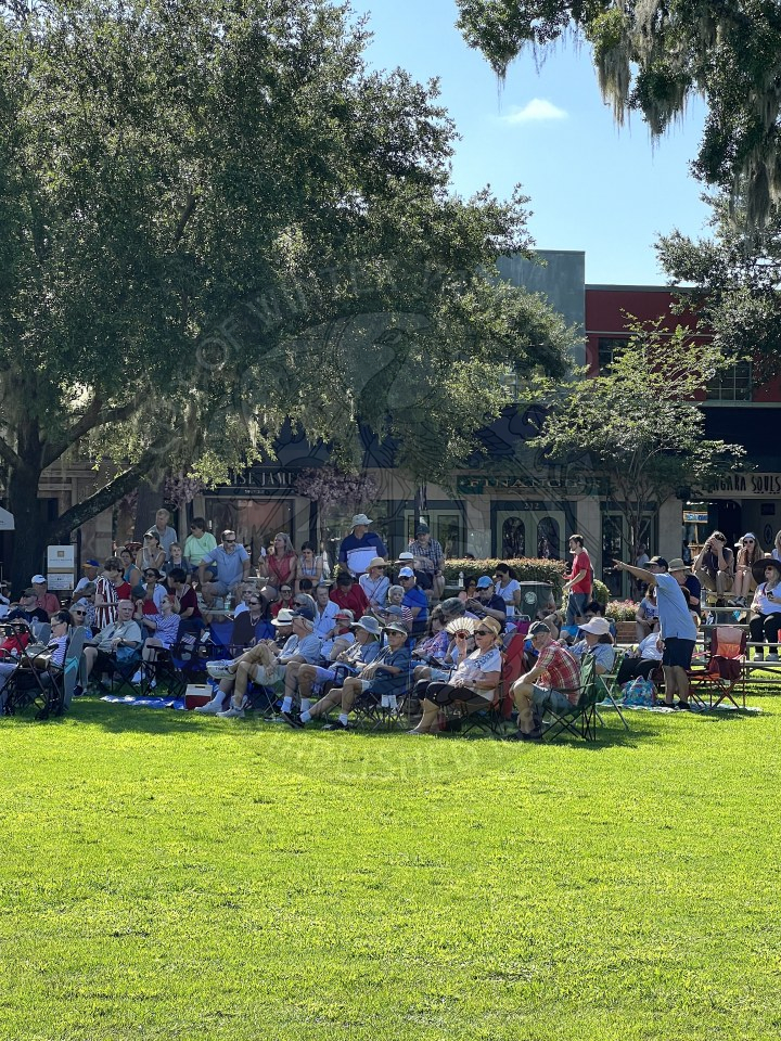 group of people sitting in lawn chairs in the shade waiting for the bach festival to start performing