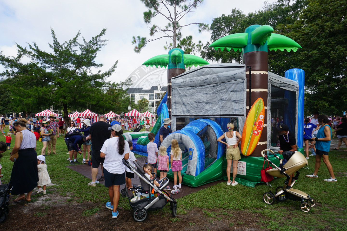 an island themed bounce house with parents standing around it watching their kids.