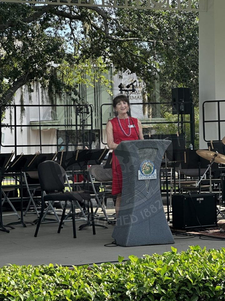 A women speaking into a mircophone standing behind a podium talking to the guests.