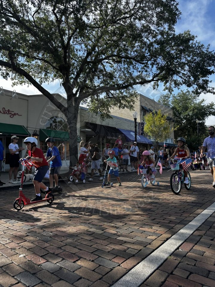 kids riding decorated fourth of july themed bikes riding on a brick road.