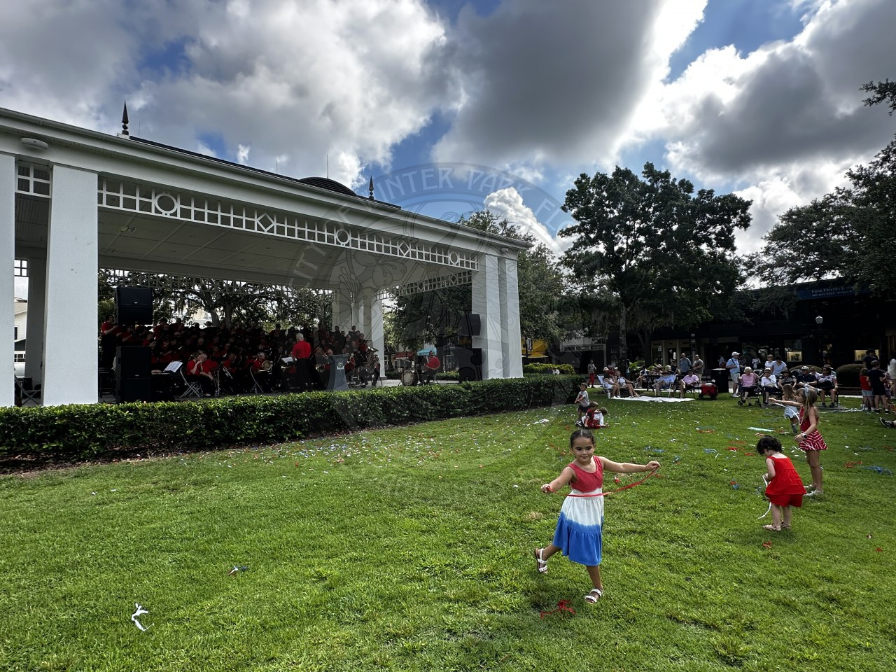 kids running around in the grass with a band on stage playing their musical instruments.