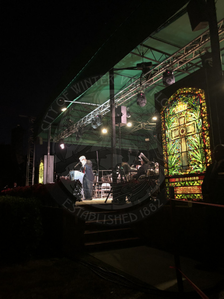 Central Park stage with a man behind a podium with a stained glass window to the right