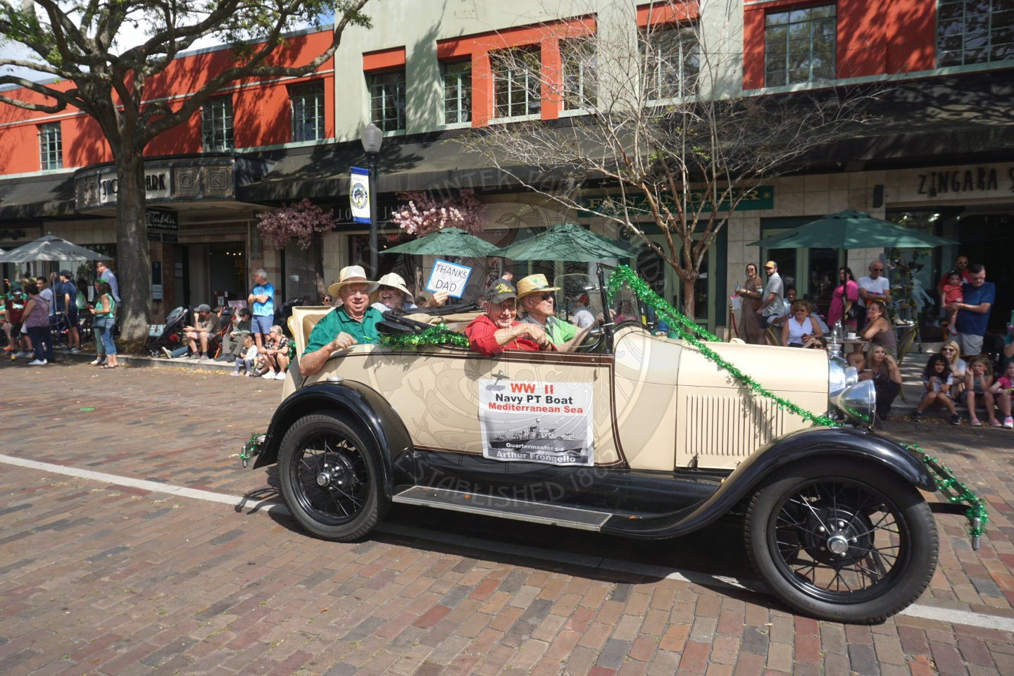 old vintage car with 4 older men waving at the people on the side of the road
