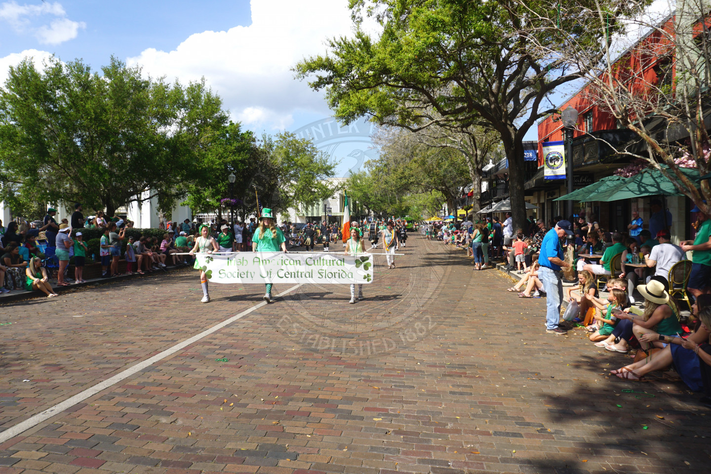 3 people holidng a banner that says "Irish American Cultural Society of Central Florida" walking down Park Avenue