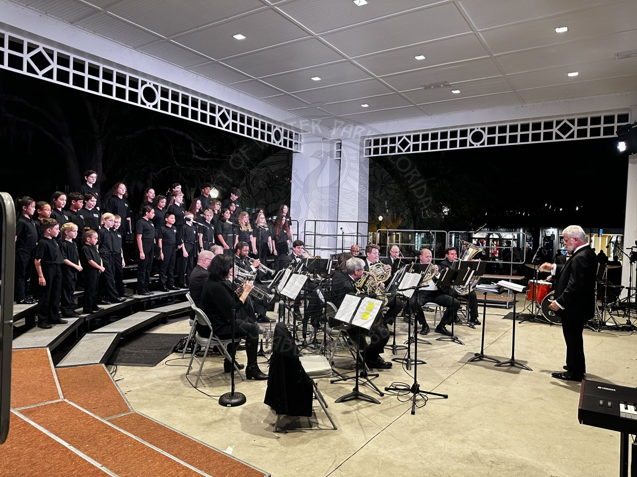 a side view of the stage of Bach performing with a director in the front waving his hands around directingt he band what to play.