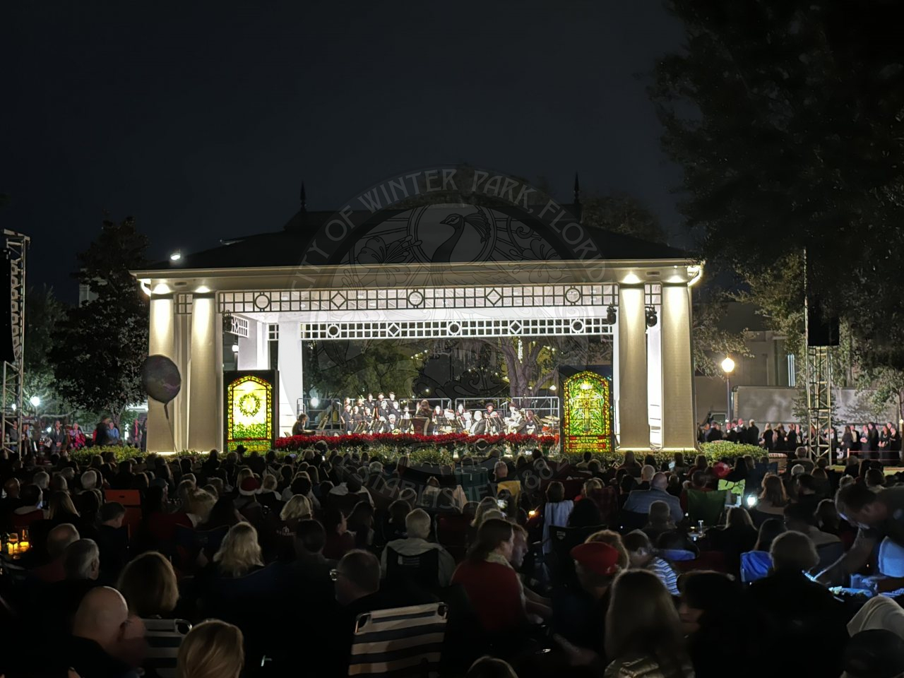 A stage with a stained glass window on each side of stage and a band seated in the middle playing instruments.