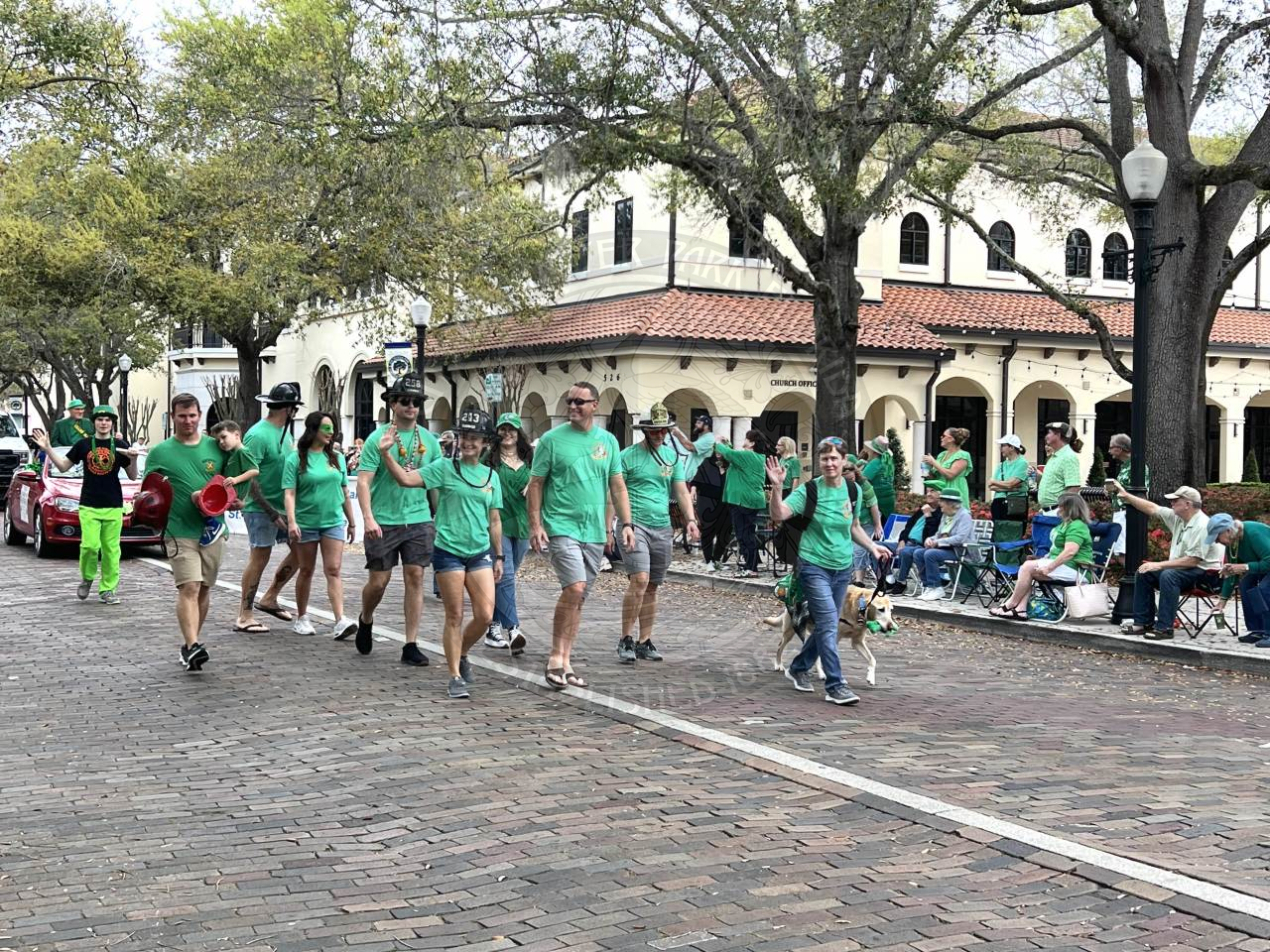 Group of people wearing green shirts and walking down Park Avenue waving at the viewers watching the parade.