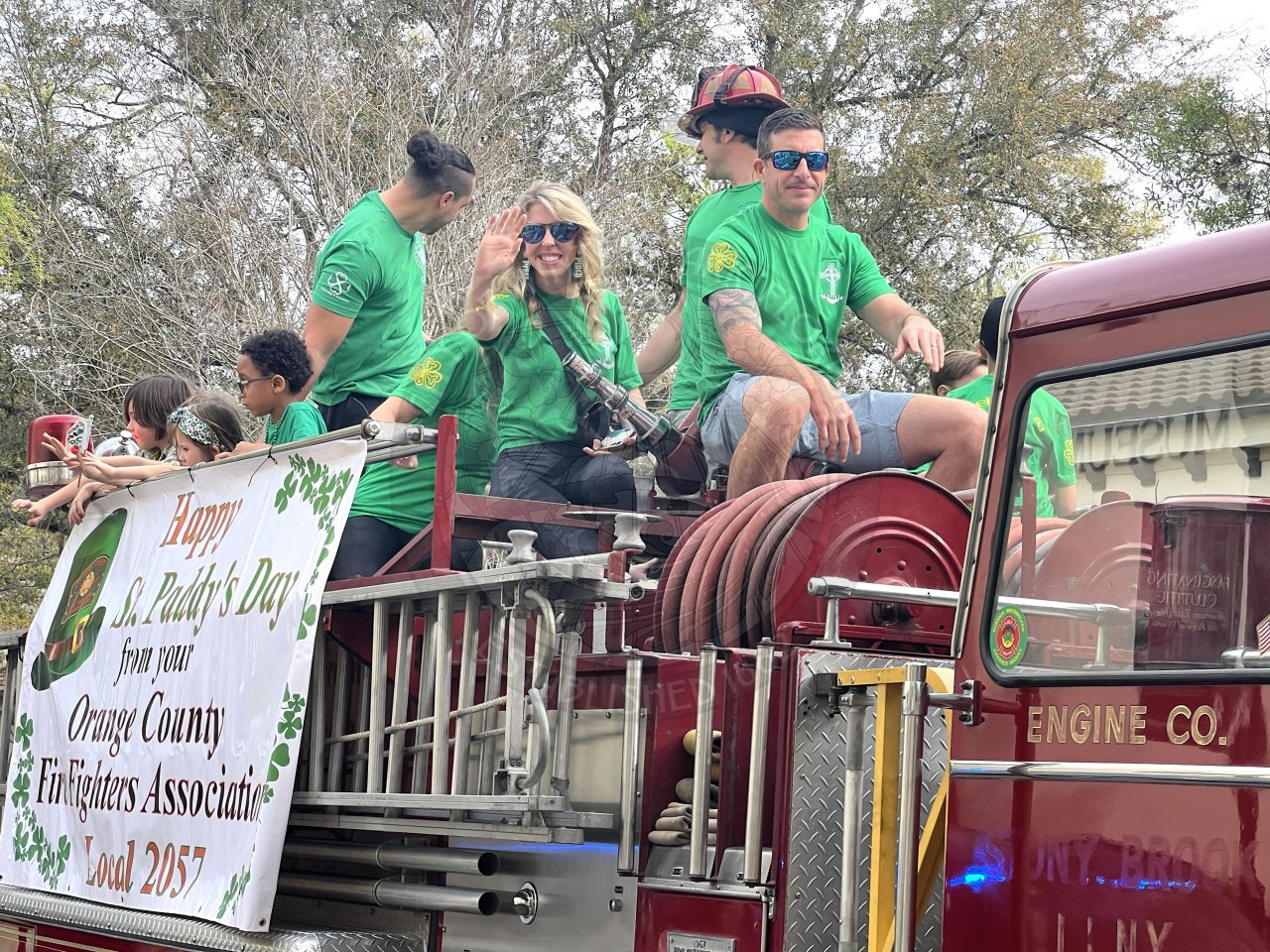 Orange County Firefighters Association banner on the side of a firetruck with men and women at the top of the  truck smiling and waiving.