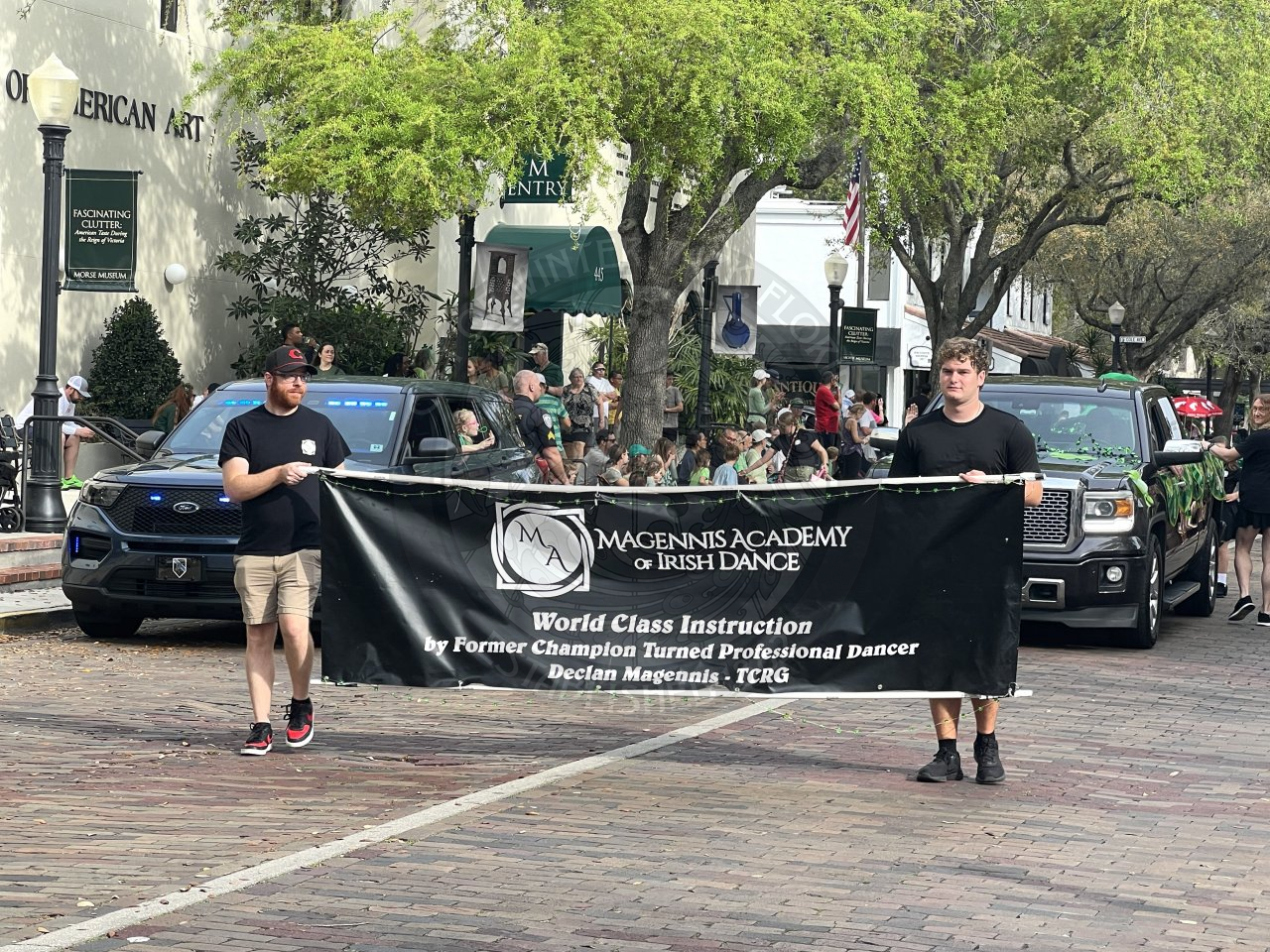 2 men holding a banner that says "Magennis Academy of Irish Dance. 