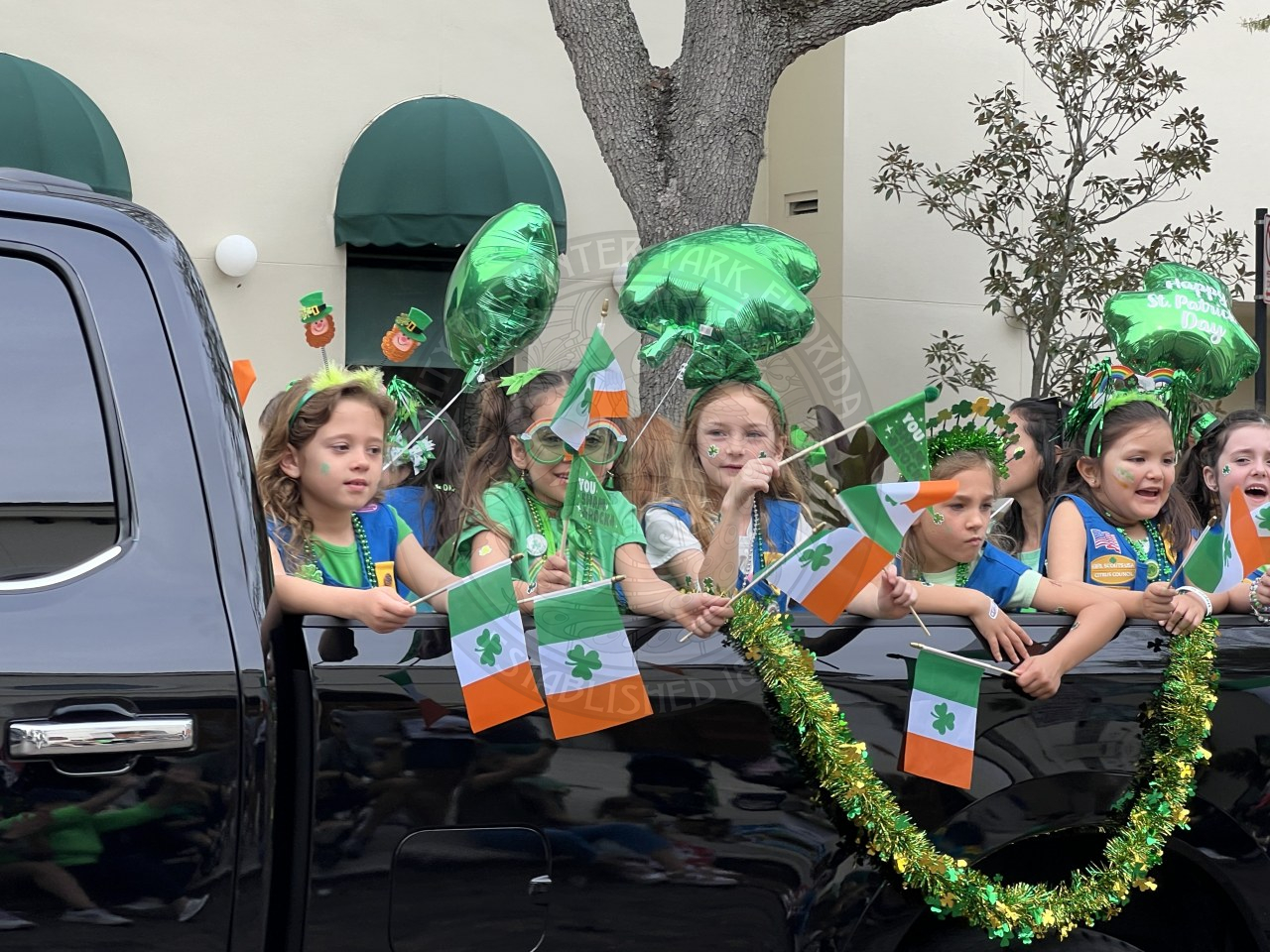 girl scouts in the trunk of a baclk truck. holding ireland flags with green shamrock balloons swaying in the wine.