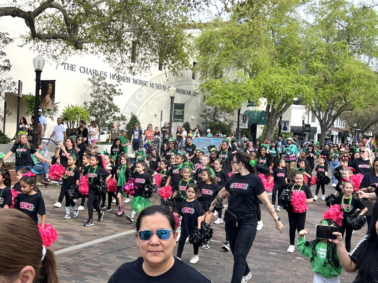 big group of kids and paretns walking down park avenue. the kids have one black and one pink pom poms in their hands.