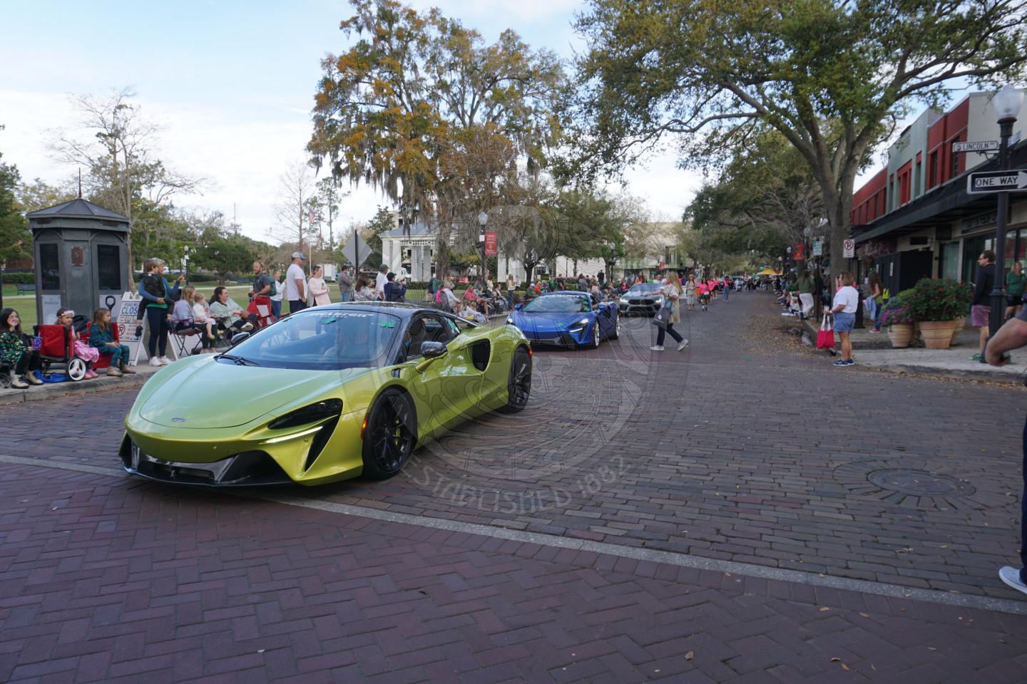 McClaren cars driving down a brick street.